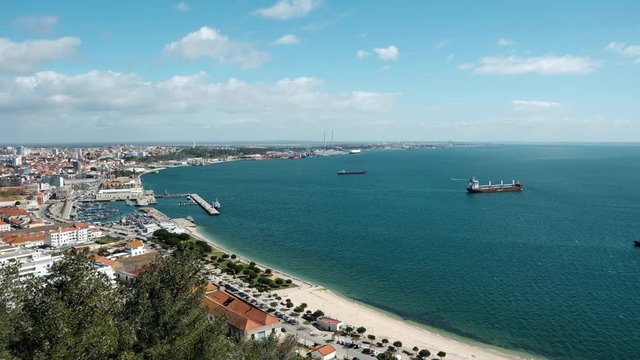 Ship moves into dock at industrial yet picturesque harbour in Portugal. Time-lapse with beach in foreground and view of bay
