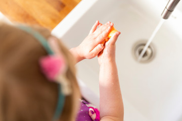 A little girl washing her hands with an orange butterfly soap