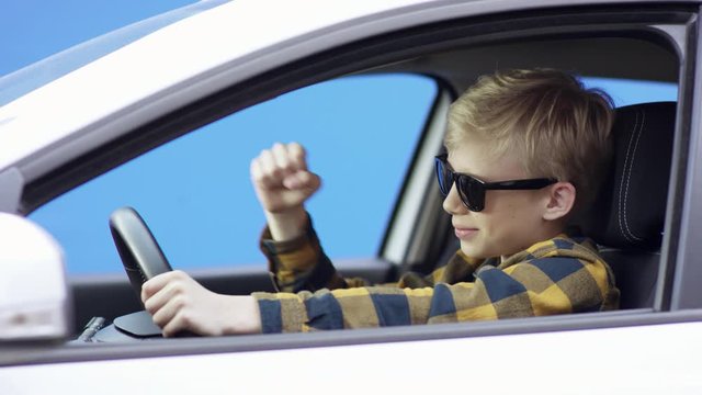 A little irritated blonde boy in casual clothes is travelling. Handsome boy is driving car with greenscreen background. He is sitting in the car. He is aruing with someone