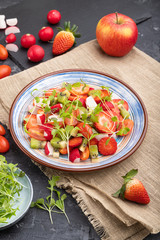 Vegetarian fruits and vegetables salad of strawberry, kiwi, tomatoes, microgreen sprouts on black concrete background. Side view.