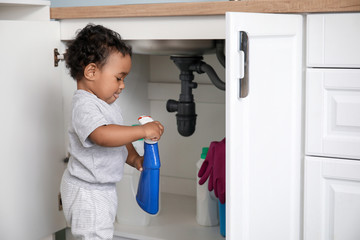 Fototapeta na wymiar Little African-American baby playing with detergents at home. Child in danger