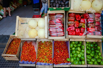 Street market vendor with groceries. Vegetables and fruits in wooden boxes outside on the street near store. Red pepper, cherry tomatoes, melon and small green pumpkins. Buenos Aires, Argentina.
