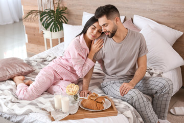 Young couple with breakfast resting on bed at home