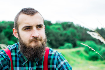 Handsome man hipster with beard on serious face in cloth shirt and suspenders sunny outdoor on mountain top against cloudy sky on natural. Tourism concept. Wonderful landscape.