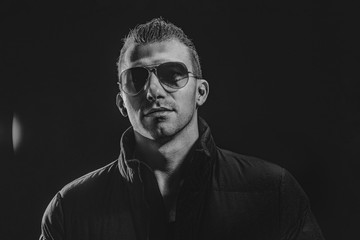 Obraz premium Black and White Brutal confident strong beautiful male model in glasses on isolated dark background.