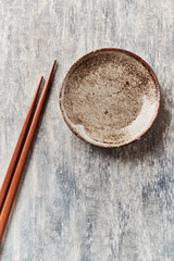 Wooden chopsticks and empty ceramics plate on rustic wooden background. Top view. Copy space.