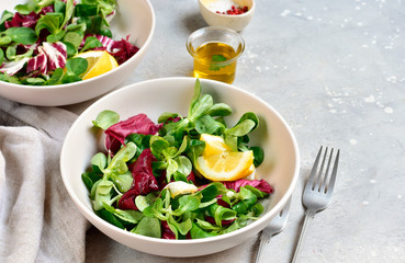 diet salad from radicchio, arugula, valerian leaves with lemon and olive oil in a white bowl on a gray background. vitamin diet salad recipe. selective focus, copy space