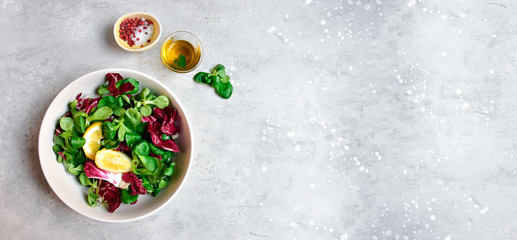 banner diet salad from radicchio, arugula, valerian leaves with lemon and olive oil in a white bowl on a gray background. vitamin diet salad recipe. selective focus, copy space