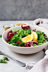 diet salad from radicchio, arugula, valerian leaves with lemon and olive oil in a white bowl on a gray background. vitamin diet salad recipe. selective focus, copy space