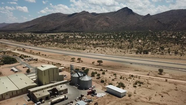 4K aerial video of newly upgraded main A1/B1 highway outside Windhoek to town Okahandja with bush covered mountains, dry endless savanna view, metal silo towers in Khomas Region, central Namibia