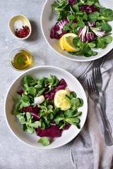 diet salad from radicchio, arugula, valerian leaves with lemon and olive oil in a white bowl on a gray background. vitamin diet salad recipe. selective focus, copy space