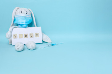 Fototapeta na wymiar Children's soft toy bunny in a protective medical mask holds the inscription virus, medical syringe on a blue background.