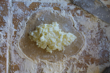 Stage of preparation of Karelian pies -Pirakka. Pies are located on a wooden board, being filled ready for baking. Dish of national cuisine - piirakka. Close-up.