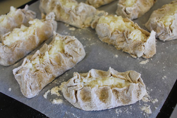 Stage of preparation of Karelian pies -Pirakka. Pies are located on a wooden board, being filled ready for baking. Dish of national cuisine - piirakka. Close-up.