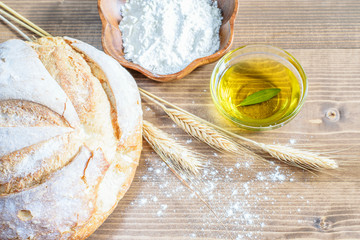 Loaf of white round bread with wheat ears, flour and olive oil on the kitchen wooden table. Natural homemade white bread.