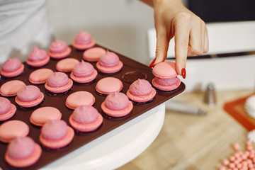 Confectioner in a kitchen. Woman in a uniform. Professional decorates the macaroni.