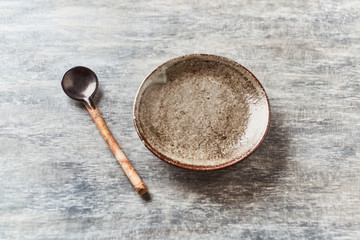 Empty ceramics plate and spoon on rustic wooden background.  Copy space.