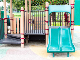 empty green plastic double slide with metal steps in a closed children's outdoor playground