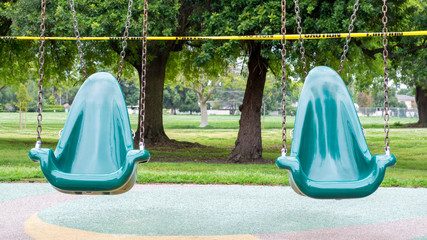 two green plastic playground swings blocked off by yellow caution tape during covid-19 lock down