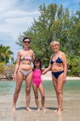 Happy family along the shoreline. Causasian woman with daughter and mother, three people smiling on the beach
