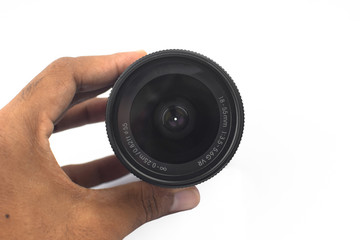 A person holding a black color camera lens of a digital camera before white background