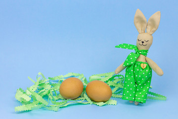 Happy Bunny toys. Easter decorations on a blue background. Eggs in a paper nest. Free space for...