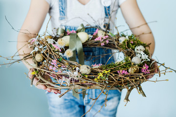 woman holding easter wreath with colorful eggs and ribbons on sky blue background © Mariia