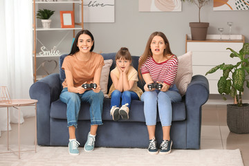 Happy lesbian couple with little adopted girl playing video game at home