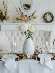 Home table setting decor. Elegant white and brown colors. Festive table for traditional holiday dinner, decorated with spring flowers, napkins and eggs. Happy easter