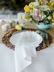 Table setting decoration. Traditional holiday dinner, white spring flowers, brown tablecloth and napkins, white plate. Decorated festive table. Easter eggs.