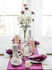 Festive table setting with marsala violet textile napkin and tablecloth, easter eggs, white dish and golden cutlery, candles and glass for wine. purple color