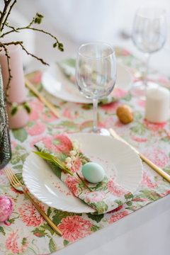 Decorative festive table setting with floral tablecloth, egg, dish and golden cutlery, glass for wine, willow branch. Happy easter holidsy concept.