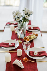 Decorative table setting with red textile, easter eggs, white dish and golden cutlery, candles and...