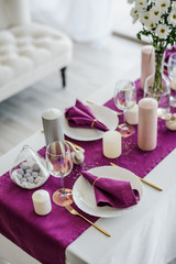 Obraz na płótnie Canvas Festive table setting with marsala violet textile napkin and tablecloth, easter eggs, white dish and golden cutlery, candles and glass for wine. purple color