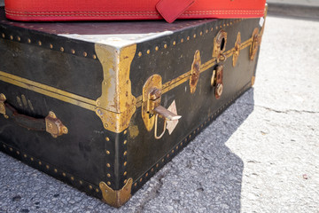 An antique bright orange stylish vintage suitcase sitting on a blue travel trunk with brass corners, lock and a handle. The hard covered retro-style suitcase has a name tag hanging down. 