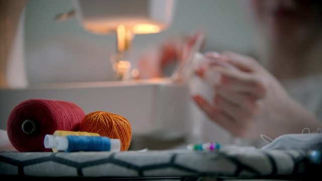 Young woman designer working with clothes and pins sitting by the sewing machine