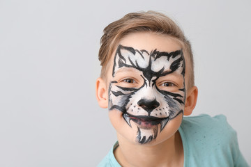 Funny little boy with face painting on light background
