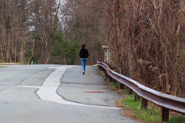 Young woman walking on a road by herself for exercise while practicing social distancing during Coronavirus pandemic 
Concepts include: solitude, social distancing, loneliness, exercise, health