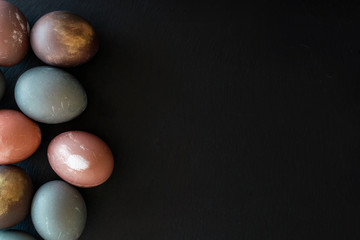 Collection of Holiday eggs on black stone   backround, natural  colorful egg painted in pastel colors on dark table. Frame with  copy space. Easter concept.