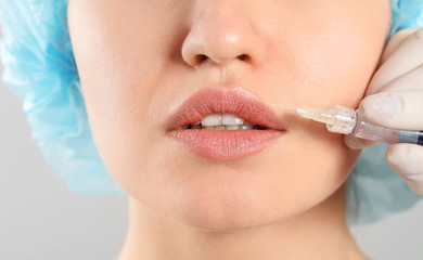 Young woman receiving filler injection on grey background, closeup
