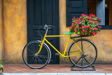 Fototapeta na wymiar Yellow vintage bike with basket full of flowers next to an old building in Danang, Vietnam