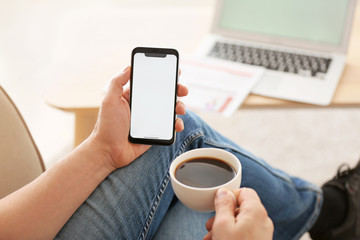 Young man with mobile phone drinking coffee at home