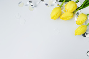 Yellow tulips and silner serpantine and confetti with space for text on grey background, flat lay, Happy Easter or woman concept. Mother greeting card