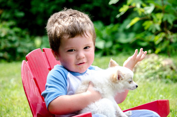 Little boy with small white dog sitting in his yard