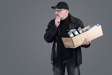 A confused man in black clothes with a box of office supplies. Dismissal from work. Loss of jobs. The shock of losing your job. The closure of the firm. Unemployment. Economic crisis.