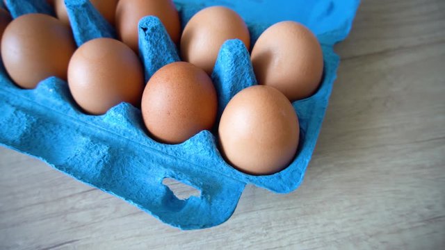 the natural organic chicken eggs of poultry in eco carton paper wrapped in blue color on a wooden table close-up