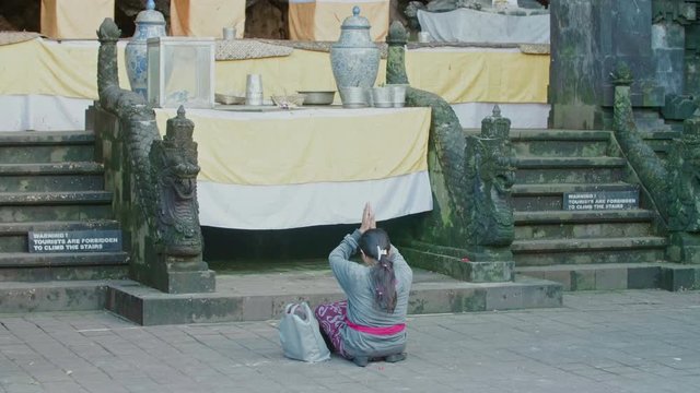Great shot of a balinese hindu woman devotee praying in front of the altar. Her hands raised above her head in prayer during the daytime in Bali, Indonesia