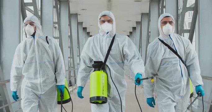 Group of professional disinfectors walking with chemical detergents