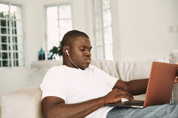 A man of African appearance at home in front of a laptop watching a movie vacation