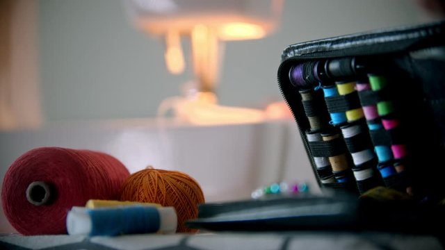 Young woman designer sewing using a sewing machine - sewing accessories on the foreground